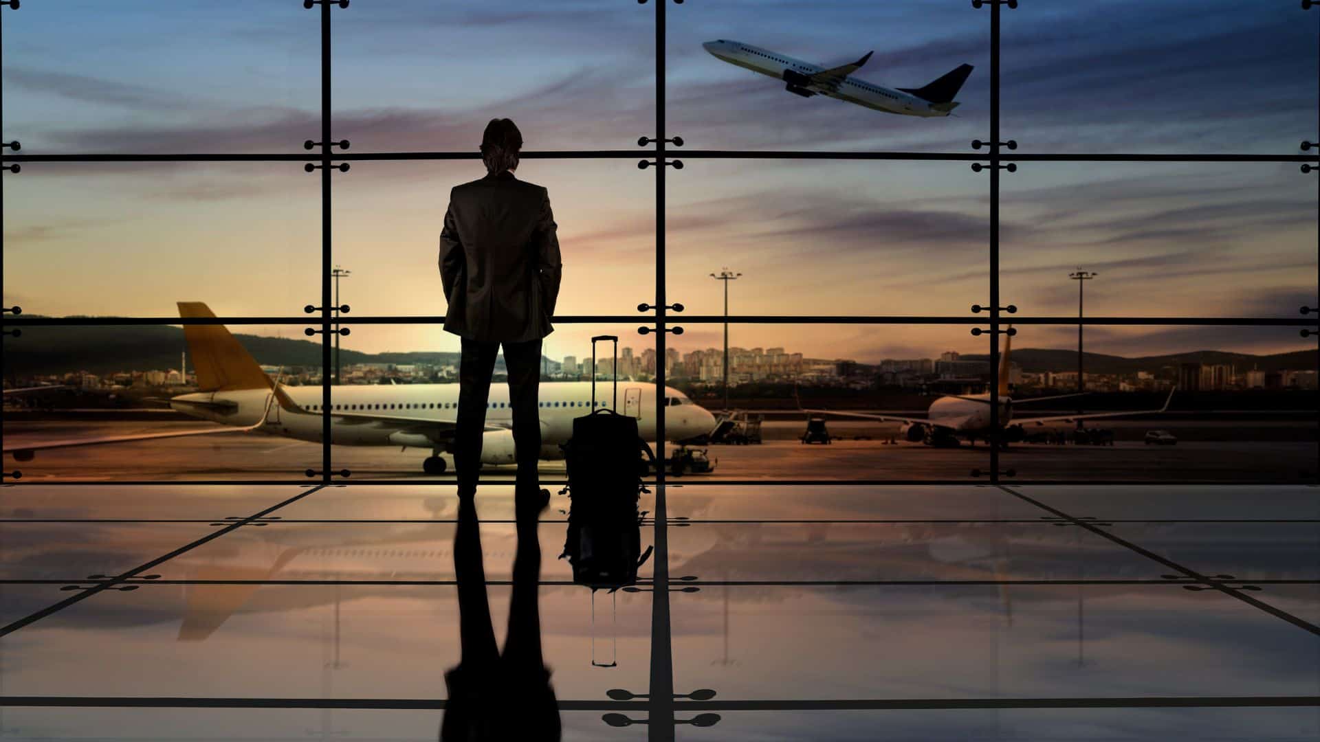 Businessman looking out from an airport at a plane taking off.