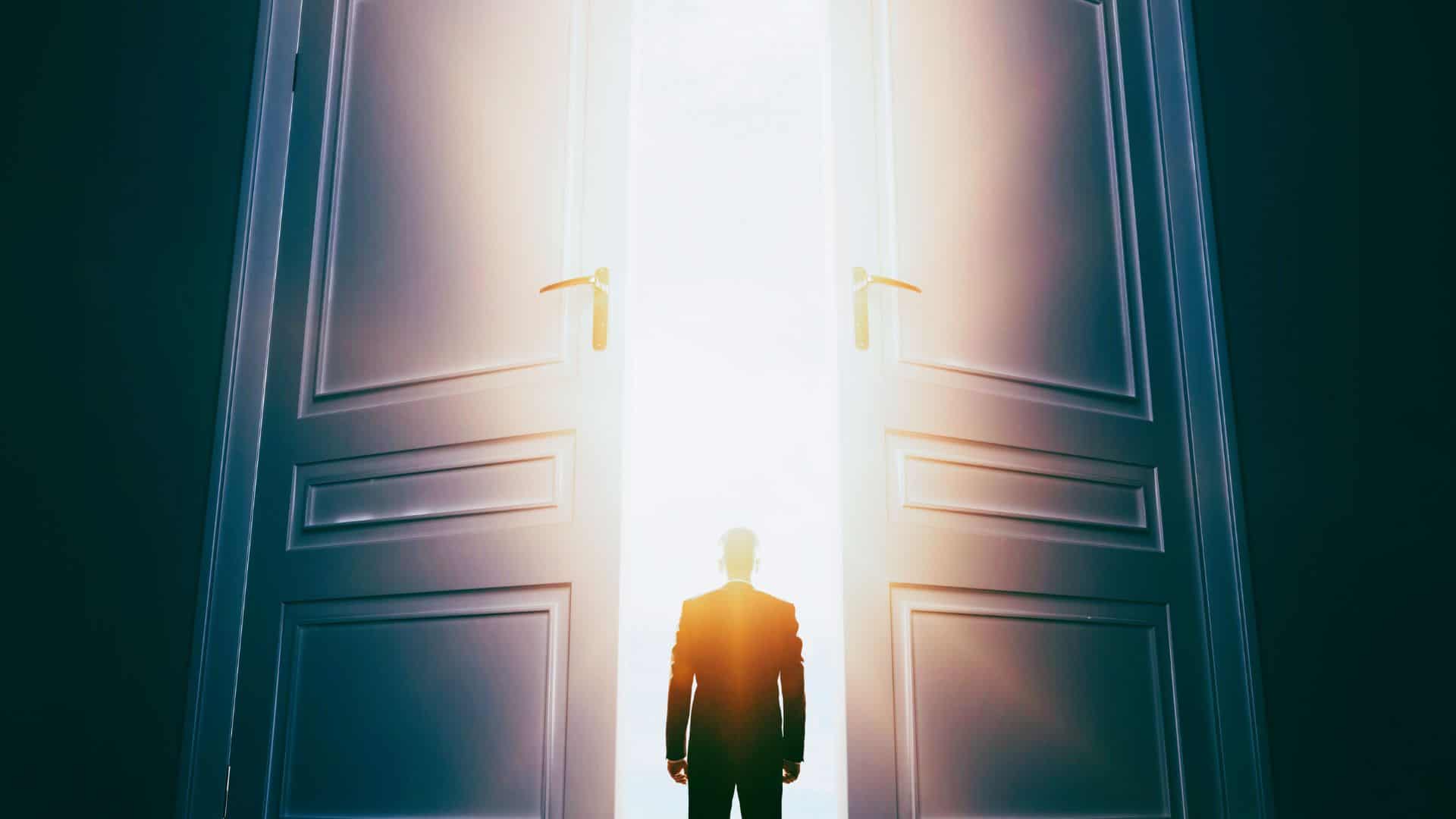 The silhouette of a business man standing in front of two large opening doors